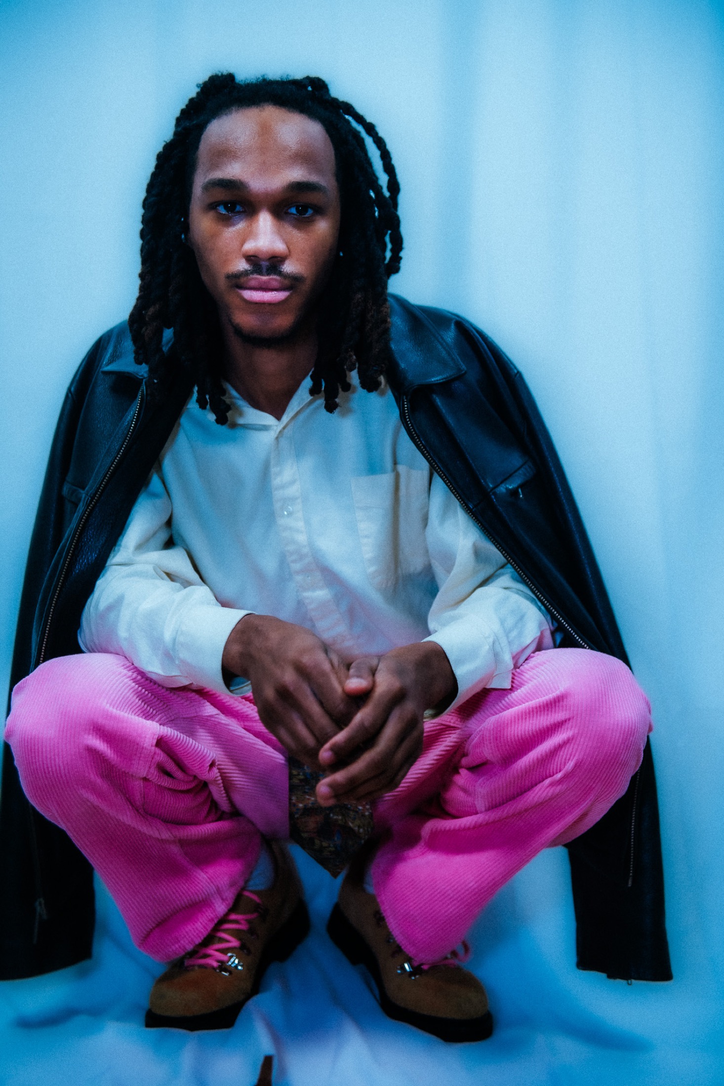 Kamari crouched in a black jacket and pink pants